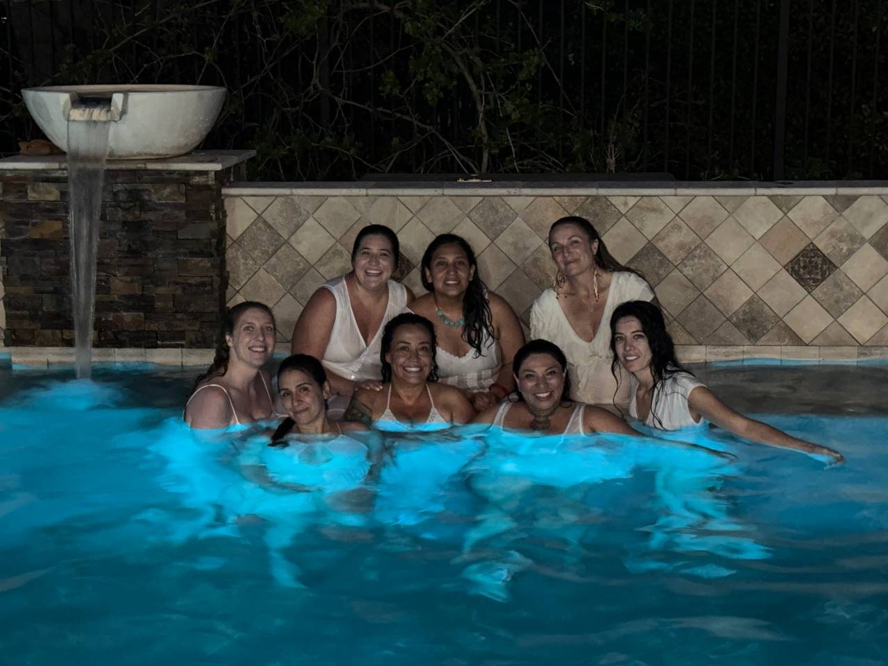 Women smiling together in a glowing pool at night