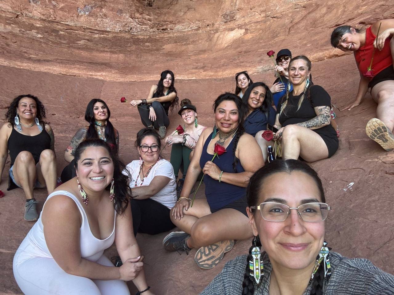 Women gathered in a red-rock alcove holding roses